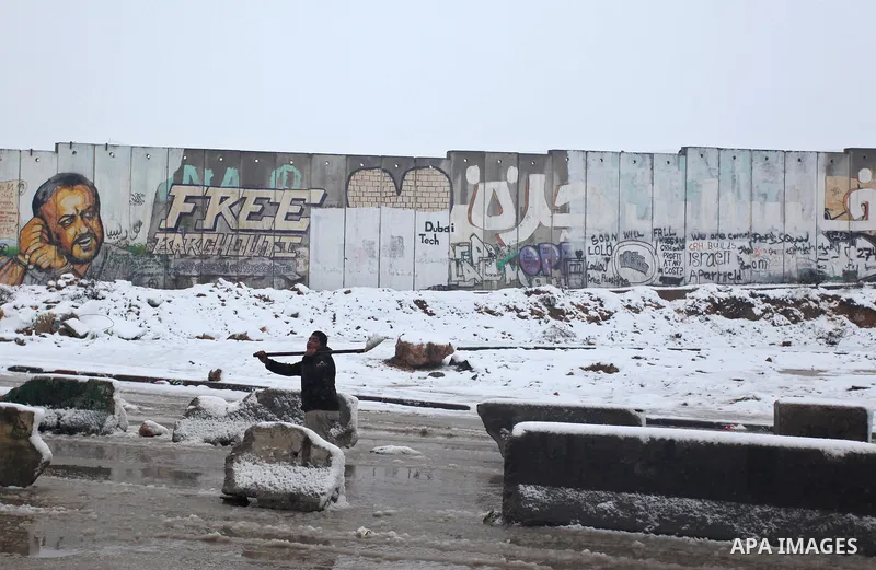 A Palestinian man tries to remove the snow next to a section of Israel's separation barrier in Qalandia between Jerusalem and the West bank city of Ramallah, Thursday, Jan. 10, 2013. Stormy weather conditions continued o...