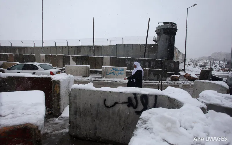 A Palestinian woman walks next to a section of Israel's separation barrier during snowfall in Qalandia between Jerusalem and the West bank city of Ramallah, Thursday, Jan. 10, 2013. Stormy weather conditions continued on...
