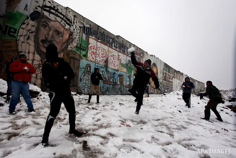 Palestinians play in the snow next to a section of Israel's separation barrier in Qalandia between Jerusalem and the West bank city of Ramallah, Thursday, Jan. 10, 2013. Stormy weather conditions continued on Thursday wi...