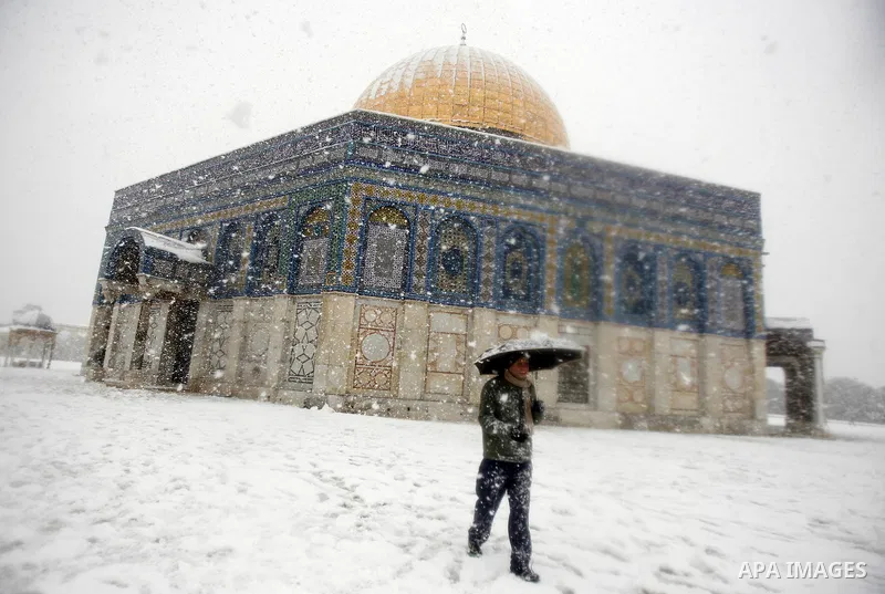 A Palestinian man walks in front of the Dome of the Rock mosue as snow falls at the Al-Aqsa mosque compound in the old city of Jerusalem on January 10, 2013. Jerusalem was transformed into a winter wonderland after heavy...