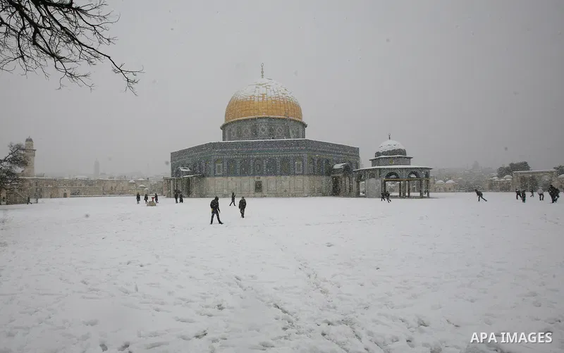 Palestinians walk in front of the Dome of the Rock mosue as snow falls at the Al-Aqsa mosque compound in the old city of Jerusalem on January 10, 2013. Jerusalem was transformed into a winter wonderland after heavy overn...