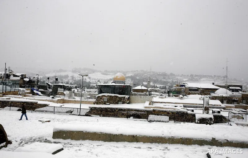 Palestinians walk in front of the Dome of the Rock mosue as snow falls at the Al-Aqsa mosque compound in the old city of Jerusalem on January 10, 2013. Jerusalem was transformed into a winter wonderland after heavy overn...