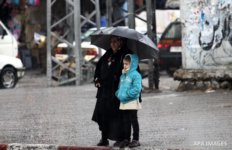 A Palestinian woman with her daughter wait to cross the street as wintry weather swept through the region, in Gaza city on 10 January 2013. Abnormal storms, which for four days have blasted the Middle East with rain, sno...