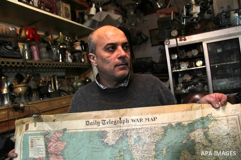 A Palestinian vendor displays an old page from the Daily Telegraph newspaper shows the map of World War II prepared by the London Geographical Institute, in his antiques store in Gaza city on January 20, 2013. Photo by E...