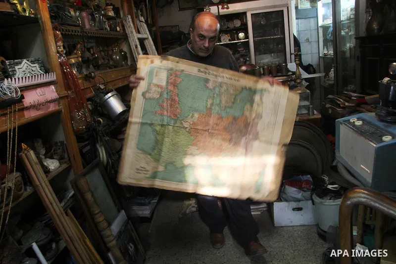 A Palestinian vendor displays an old page from the Daily Telegraph newspaper shows the map of World War II prepared by the London Geographical Institute, in his antiques store in Gaza city on January 20, 2013. Photo by E...