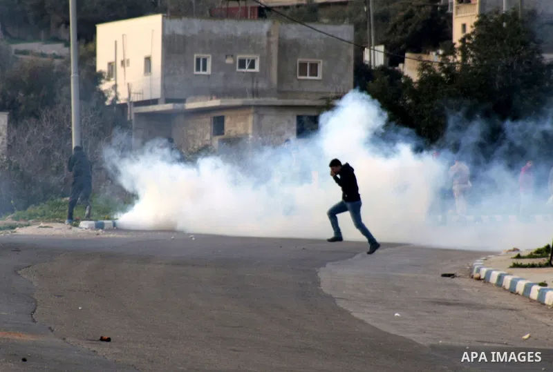 A Palestinian protester runs cover from tear gas fired by Israeli soldiers during a protest in Anin village in the West Bank near Jenin city, on January 26, 2013. Protestors planned to erect a number of tents in solidari...