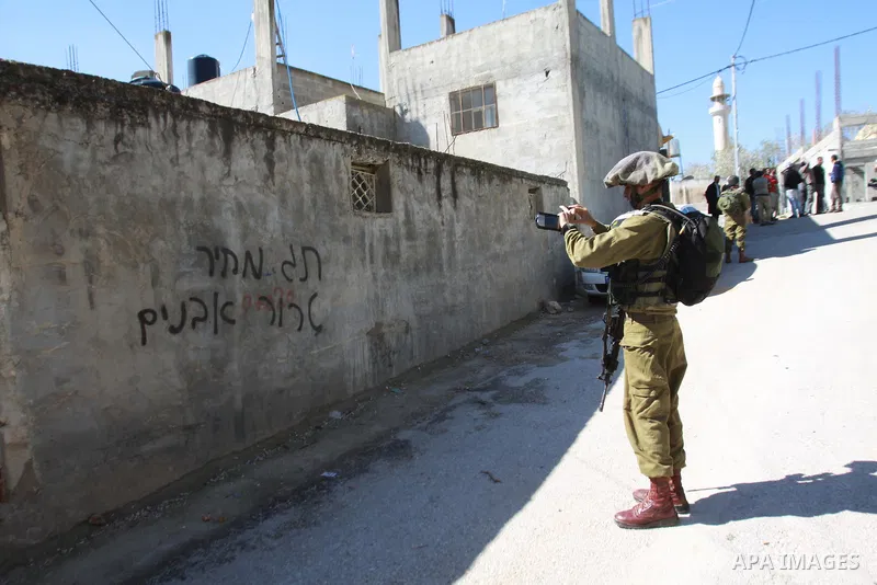 An Israeli security officer takes photo for a writing on a wall reading in Hebrow "stone throwers must pay the price" following an attack from Jewish settlers on three Palestinian cars in the West Bank village of Yasuf n...