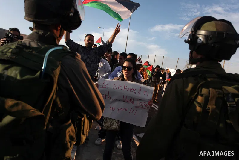 A woman holds up a sign that reads, "In Sickness and in health.. until Israel do us part", as Israeli soldiers prevent the progress of a symbolic wedding party towards the Israeli constructed controversial separation bar...