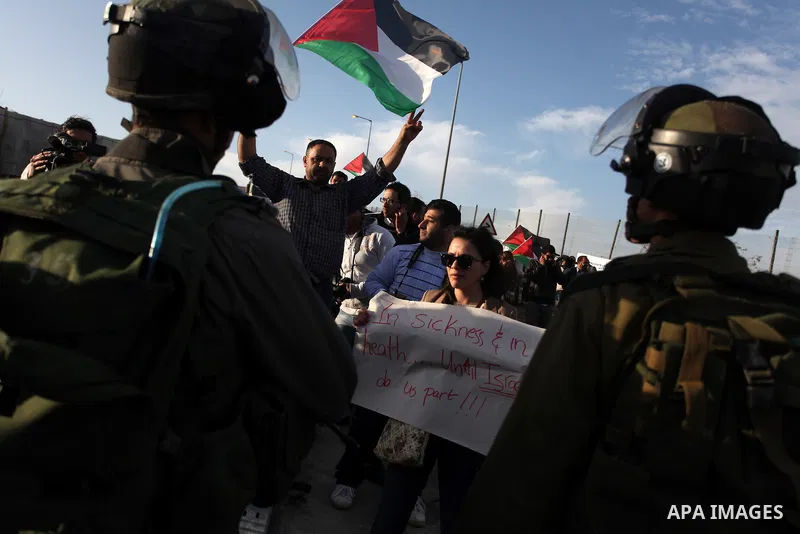 A woman holds up a sign that reads, "In Sickness and in health.. until Israel do us part", as Israeli soldiers prevent the progress of a symbolic wedding party towards the Israeli constructed controversial separation bar...