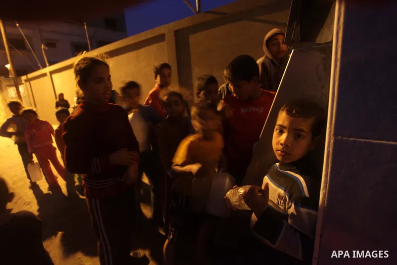Palestinian boys and girls stand in line holding container as they wait to fill with fresh water from the desalination station in Deir al-Balah refugee camp in the center of the Gaza Strip on March 26, 2013. Photo by Ash...