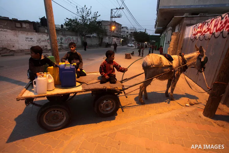 Palestinian boys and girls stand in line holding container as they wait to fill with fresh water from the desalination station in Deir al-Balah refugee camp in the center of the Gaza Strip on March 26, 2013. Photo by Ash...