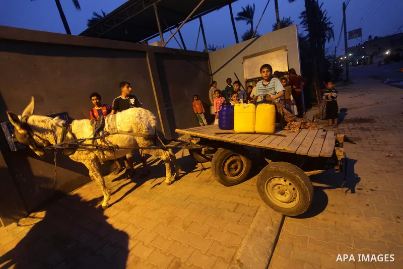 Palestinian boys and girls stand in line holding container as they wait to fill with fresh water from the desalination station in Deir al-Balah refugee camp in the center of the Gaza Strip on March 26, 2013. Photo by Ash...