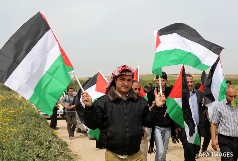 Palestinian men hold up the national flag as he walks across a field during a rally marking Land Day in Beit Hanun in the northern Gaza Strip close to the border with Israel on March 31, 2013. The annual demonstrations m...