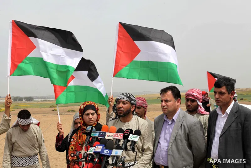 Palestinian men hold up the national flag as he walks across a field during a rally marking Land Day in Beit Hanun in the northern Gaza Strip close to the border with Israel on March 31, 2013. The annual demonstrations m...