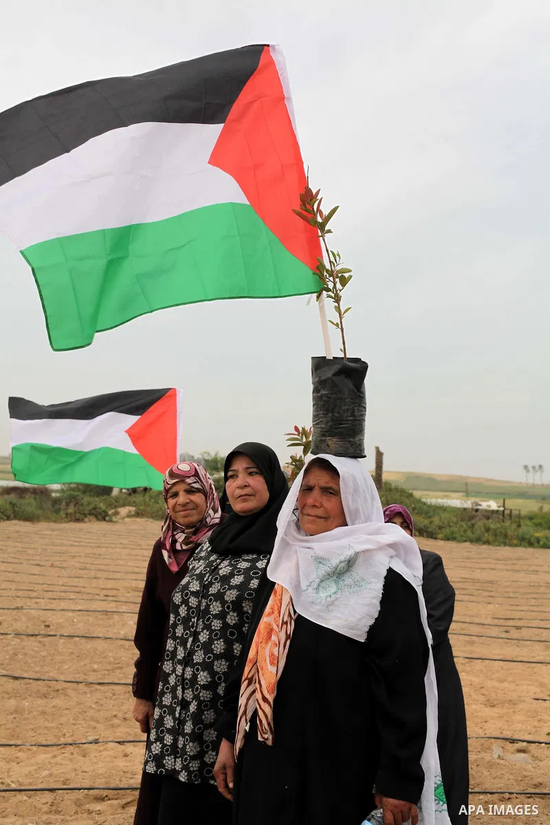 Palestinian women hold up the national flag as he walks across a field during a rally marking Land Day in Beit Hanun in the northern Gaza Strip close to the border with Israel on March 31, 2013. The annual demonstrations...