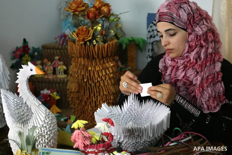 A Palestinian woman, 26-year-old Fadia Zahdeh, works on paper decorations that she created through the re-use of waste paper, to sell as gifts and to establish a small business, in the West Bank city of Hebron on May 23,...