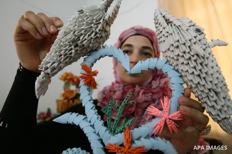 A Palestinian woman, 26-year-old Fadia Zahdeh, works on paper decorations that she created through the re-use of waste paper, to sell as gifts and to establish a small business, in the West Bank city of Hebron on May 23,...