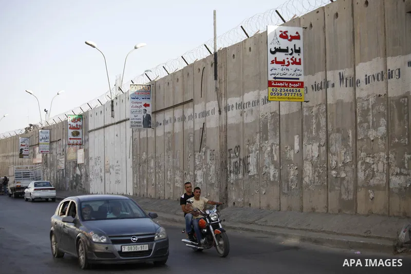 Palestinian ride their motorcycle next to the Israeli separation wall in Jerusalem on July 9, 2013. The Israeli Coordinator of Government Activities in the Territories (COGAT) announced in a press statement that Palestin...