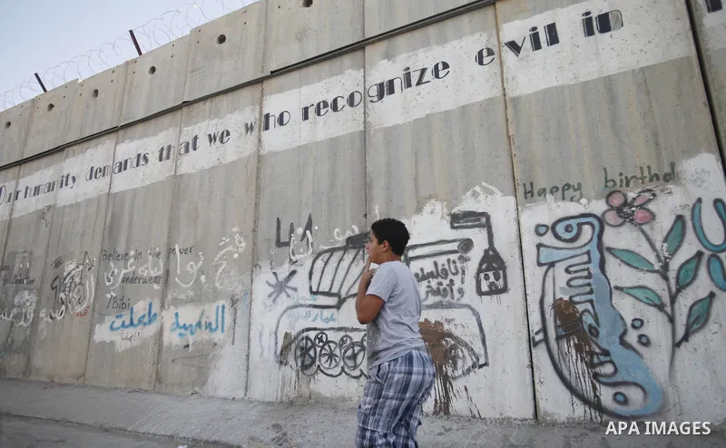 A Palestinian boy walks next to the Israeli separation wall in Jerusalem on July 9, 2013. The Israeli Coordinator of Government Activities in the Territories (COGAT) announced in a press statement that Palestinian men an...