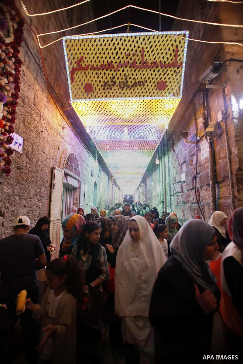 Palestinians walk in an illuminated street before attending the Taraweeh prayer at the al-Aqsa mosque compound in the old city of Jerusalem after breaking the fast on the First day of the Moslem holy month of Ramadan on...