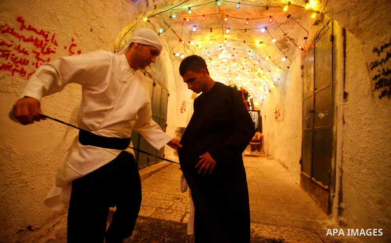 A Palestinian dawn awakener, al-Musaharati in Arabic, adjusts his colleague uniform before walk through streets to wake up Muslims for a meal before sunrise during the fasting month of Ramadan, in Jerusalem's old city on...