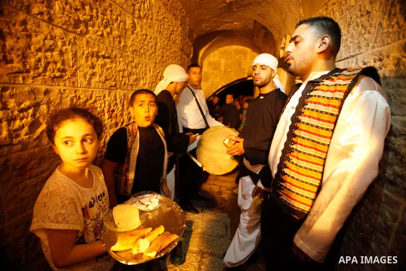 A Palestinian girl serves bread and cheese for dawn awakeners, al-Musaharati in Arabic, as they walk through streets to wake up Muslims for a meal before sunrise during the fasting month of Ramadan, in Jerusalem's old ci...