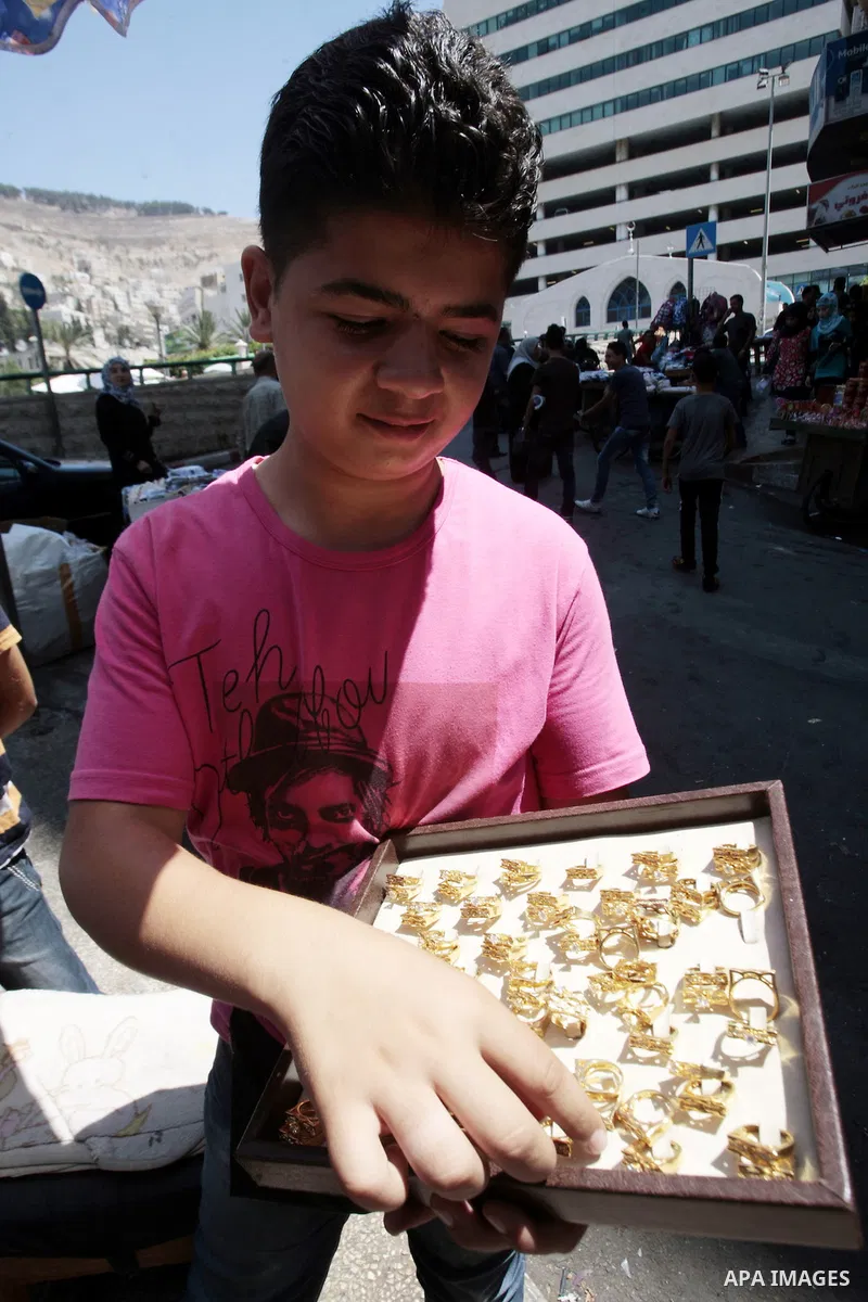 A Palestinian boy sells imitation jewelry which resembles gold at a street market in the West Bank city of Nablus, Aug 19, 2013. With gold prices soaring and high unemployment rate in Palestinian territories, imitation j...