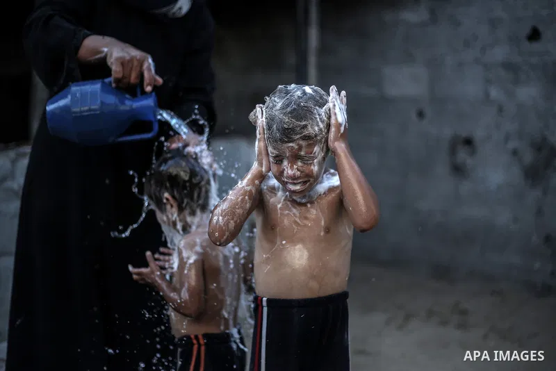 A picture taken on July 31, 2013 shows a Palestinian woman bathing her sons in front of their home in Jabalia refugee camp northern Gaza Strip. Photo by Mahmoud Hamda