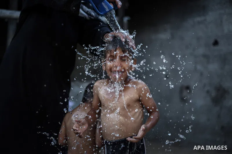 A picture taken on July 31, 2013 shows a Palestinian woman bathing her sons in front of their home in Jabalia refugee camp northern Gaza Strip. Photo by Mahmoud Hamda