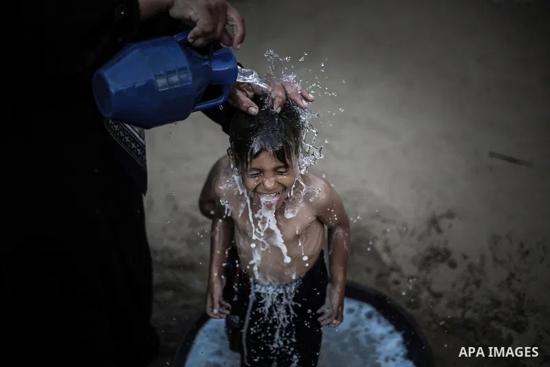 A picture taken on July 31, 2013 shows a Palestinian woman bathing her sons in front of their home in Jabalia refugee camp northern Gaza Strip. Photo by Mahmoud Hamda