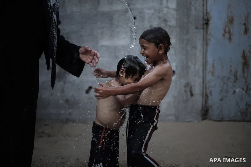 A picture taken on July 31, 2013 shows a Palestinian woman bathing her sons in front of their home in Jabalia refugee camp northern Gaza Strip. Photo by Mahmoud Hamda