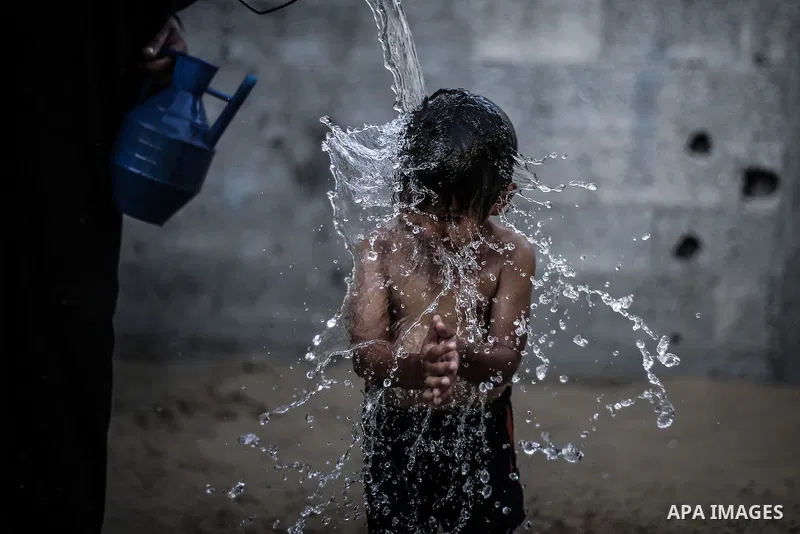 A picture taken on July 31, 2013 shows a Palestinian woman bathing her sons in front of their home in Jabalia refugee camp northern Gaza Strip. Photo by Mahmoud Hamda