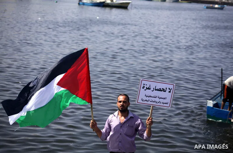 Palestinian fishermen hold banners flags during a rally inside the port of Gaza to protest on the Israeli siege on the Gaza Strip and the five-year anniversary of the entry of first two ships solidarity with Gaza, in Gaz...