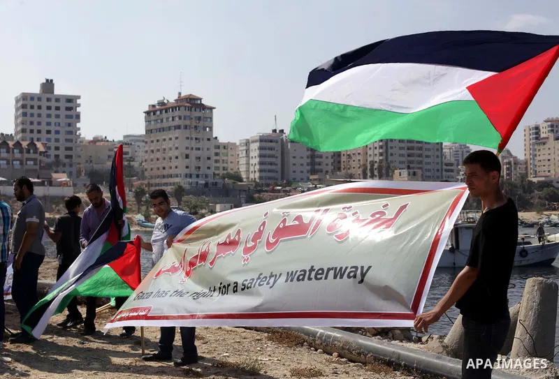 Palestinian fishermen hold banners flags during a rally inside the port of Gaza to protest on the Israeli siege on the Gaza Strip and the five-year anniversary of the entry of first two ships solidarity with Gaza, in Gaz...