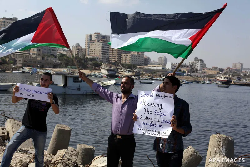 Palestinian fishermen hold banners flags during a rally inside the port of Gaza to protest on the Israeli siege on the Gaza Strip and the five-year anniversary of the entry of first two ships solidarity with Gaza, in Gaz...