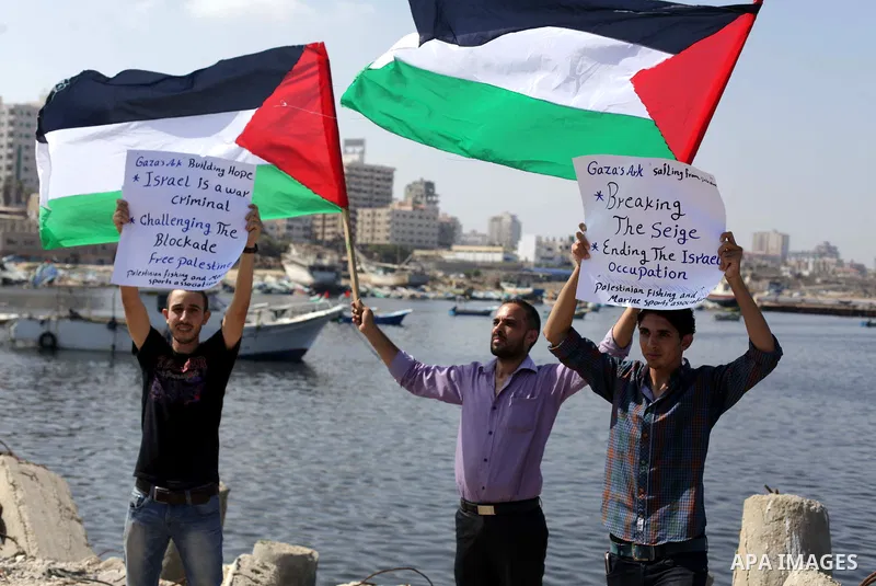 Palestinian fishermen hold banners flags during a rally inside the port of Gaza to protest on the Israeli siege on the Gaza Strip and the five-year anniversary of the entry of first two ships solidarity with Gaza, in Gaz...
