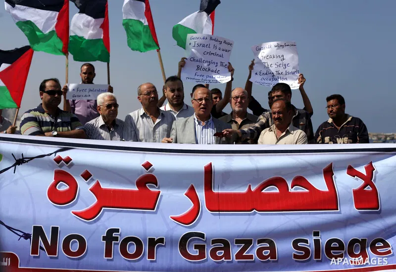 Palestinian fishermen hold banners flags during a rally inside the port of Gaza to protest on the Israeli siege on the Gaza Strip and the five-year anniversary of the entry of first two ships solidarity with Gaza, in Gaz...