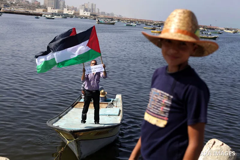 Palestinian fishermen hold banners flags during a rally inside the port of Gaza to protest on the Israeli siege on the Gaza Strip and the five-year anniversary of the entry of first two ships solidarity with Gaza, in Gaz...
