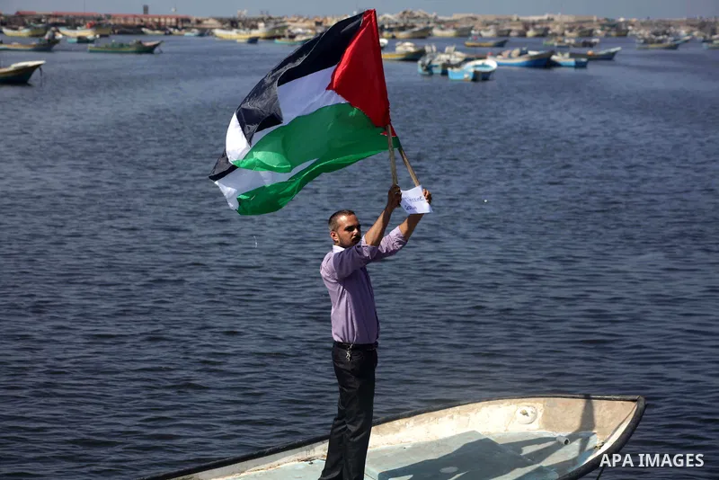 Palestinian fishermen hold banners flags during a rally inside the port of Gaza to protest on the Israeli siege on the Gaza Strip and the five-year anniversary of the entry of first two ships solidarity with Gaza, in Gaz...