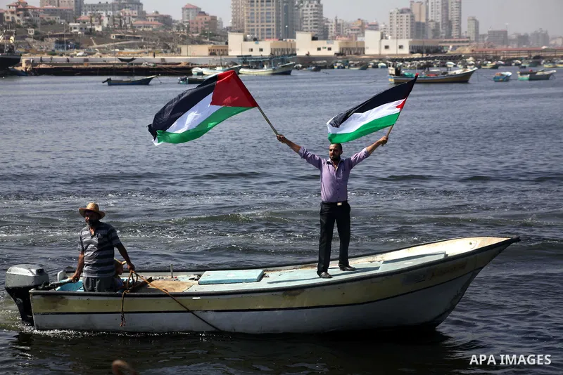 Palestinian fishermen hold banners flags during a rally inside the port of Gaza to protest on the Israeli siege on the Gaza Strip and the five-year anniversary of the entry of first two ships solidarity with Gaza, in Gaz...