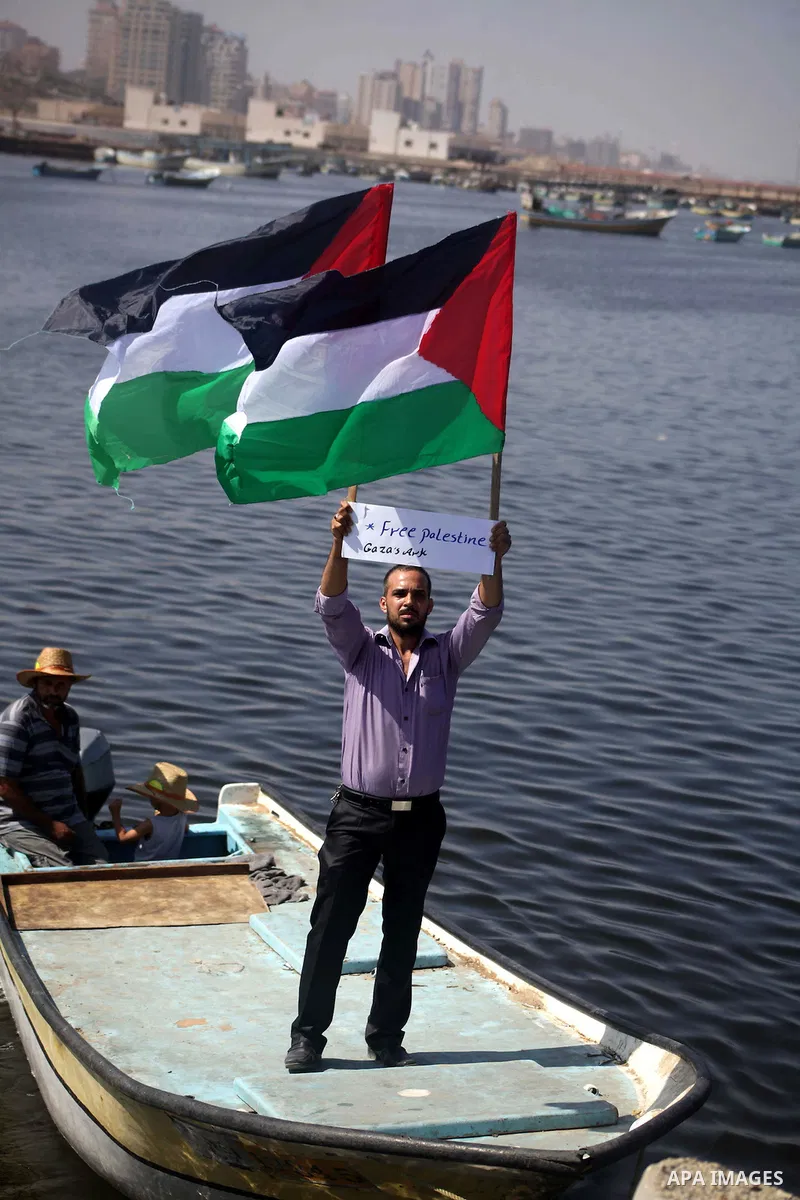 Palestinian fishermen hold banners flags during a rally inside the port of Gaza to protest on the Israeli siege on the Gaza Strip and the five-year anniversary of the entry of first two ships solidarity with Gaza, in Gaz...