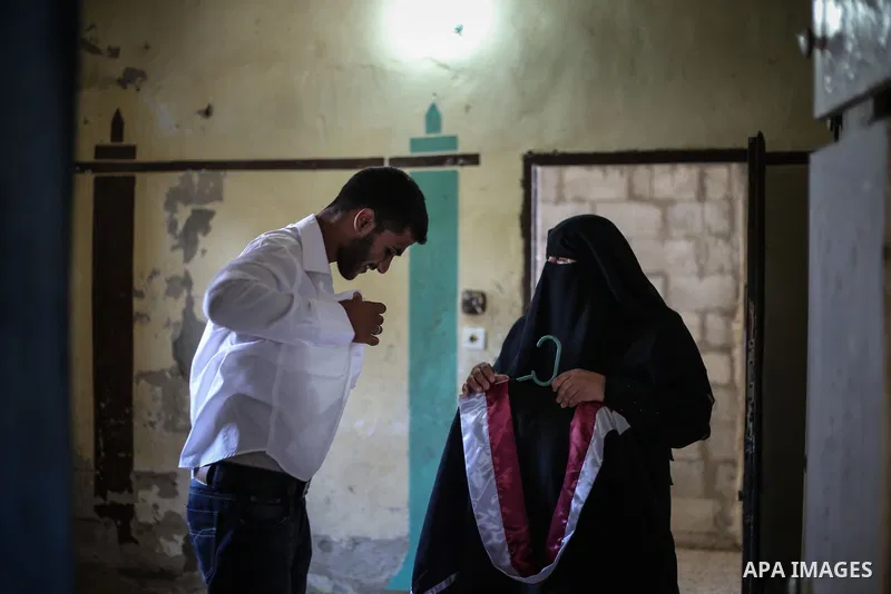 The mother of Fadi al-Shami, 21, a Palestinian blind youth, helps her son to wear his graduation suit at their home in Central Gaza Strip on Aug 17, 2013. al-Shami lost his sight after he was injured by an Israeli airstr...
