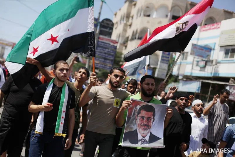 Palestinians hold up Egyptian national flags and posters of ousted Egyptian President Mohamed Morsi, during a demonstration to support Morsi and denounce Syria's President Bashar al-Assad, in Al-Nusirat refugee camp in c...