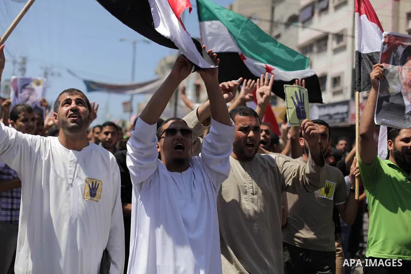 Palestinians hold Egyptian national flags, posters of ousted Egyptian President Mohamed Morsi and logos of four fingers, during a demonstration to support Morsi and denounce Syria's President Bashar al-Assad, in Al-Nusir...