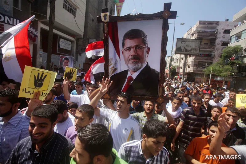 Palestinians hold Egyptian national flags, posters of ousted Egyptian President Mohamed Morsi and logos of four fingers, during a demonstration to support Morsi and denounce Syria's President Bashar al-Assad, in Al-Nusir...