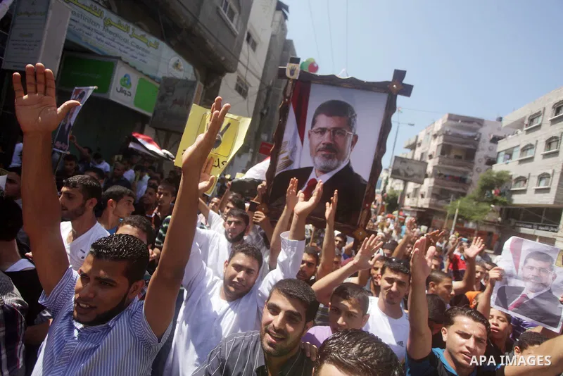 Palestinians hold Egyptian national flags, posters of ousted Egyptian President Mohamed Morsi and logos of four fingers, during a demonstration to support Morsi and denounce Syria's President Bashar al-Assad, in Al-Nusir...