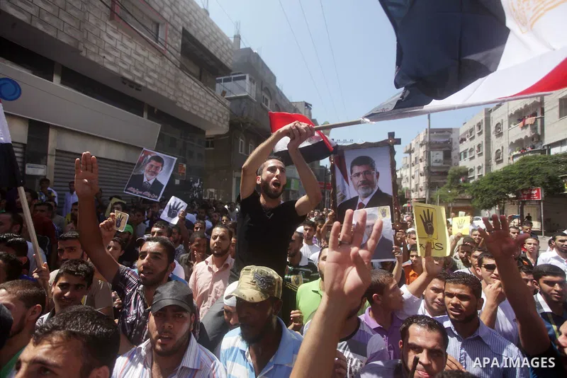 Palestinians hold Egyptian national flags, posters of ousted Egyptian President Mohamed Morsi and logos of four fingers, during a demonstration to support Morsi and denounce Syria's President Bashar al-Assad, in Al-Nusir...
