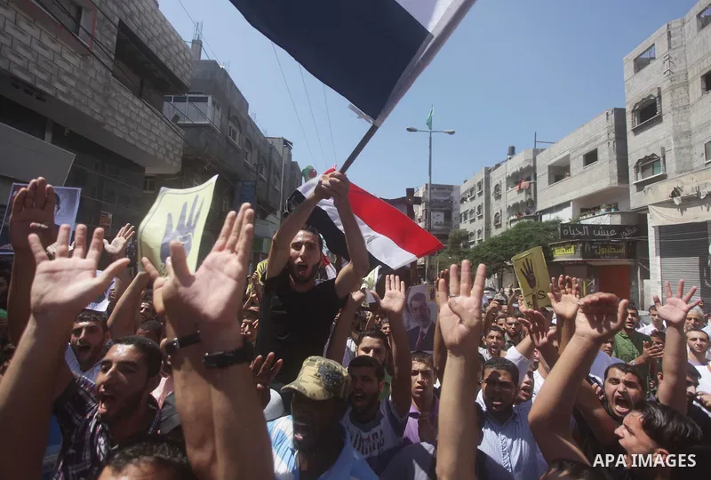 Palestinians hold Egyptian national flags, posters of ousted Egyptian President Mohamed Morsi and logos of four fingers, during a demonstration to support Morsi and denounce Syria's President Bashar al-Assad, in Al-Nusir...