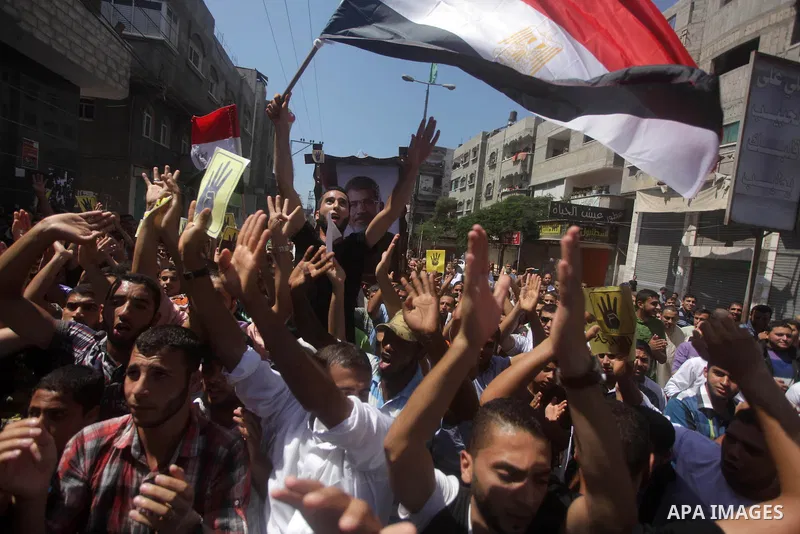 Palestinians hold Egyptian national flags, posters of ousted Egyptian President Mohamed Morsi and logos of four fingers, during a demonstration to support Morsi and denounce Syria's President Bashar al-Assad, in Al-Nusir...