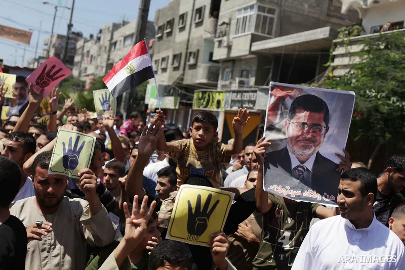 Palestinians hold Egyptian national flags, posters of ousted Egyptian President Mohamed Morsi and logos of four fingers, during a demonstration to support Morsi and denounce Syria's President Bashar al-Assad, in Al-Nusir...